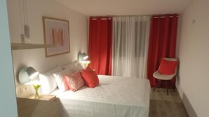 Un dormitorio con cama, lámparas de noche, una silla y una ventana con cortinas.