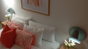Un dormitorio ordenado con una cama, almohadas, una mesita de noche con una lámpara y un aplique de pared.
