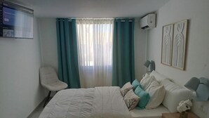 Un dormitorio con cama, una silla, una mesita de noche y una ventana con cortinas.