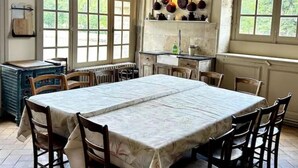 A rustic dining room with a large table, wooden chairs, and a kitchen area with hanging pots. - Chambre Lucullus - A night in the heart of the castle (La Ferté-Saint-Aubin)