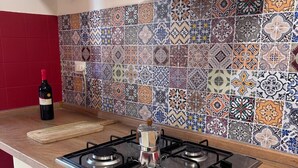 A kitchen with a gas stove, a coffee pot, and a wine bottle on the counter. - Cinecittà Family House metro A - Rome Collection  Metro A Cinecittà Roma (Roma)