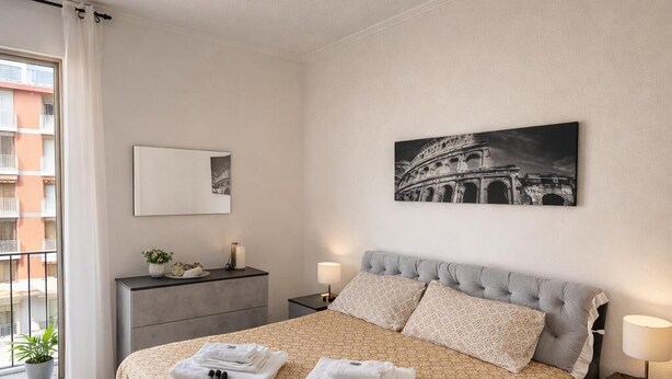 A modern bedroom with a large bed, a bedside table with a lamp, a small bedside table with a lamp, a framed picture on the wall, and a view of the outside balcony. - Cinecittà Family House metro A - Rome Collection  Metro A Cinecittà Roma (Roma)