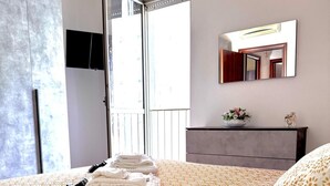 A hotel room with a bed, a bedside table with a vase of flowers, a large window, and a door leading to a balcony. - Cinecittà Family House metro A - Rome Collection  Metro A Cinecittà Roma (Roma)
