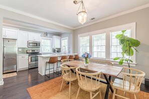 A modern kitchen with white cabinets, stainless steel appliances, and a wooden dining table with chairs. - Luxury 5BR Retreat with Private Pool (College Park)