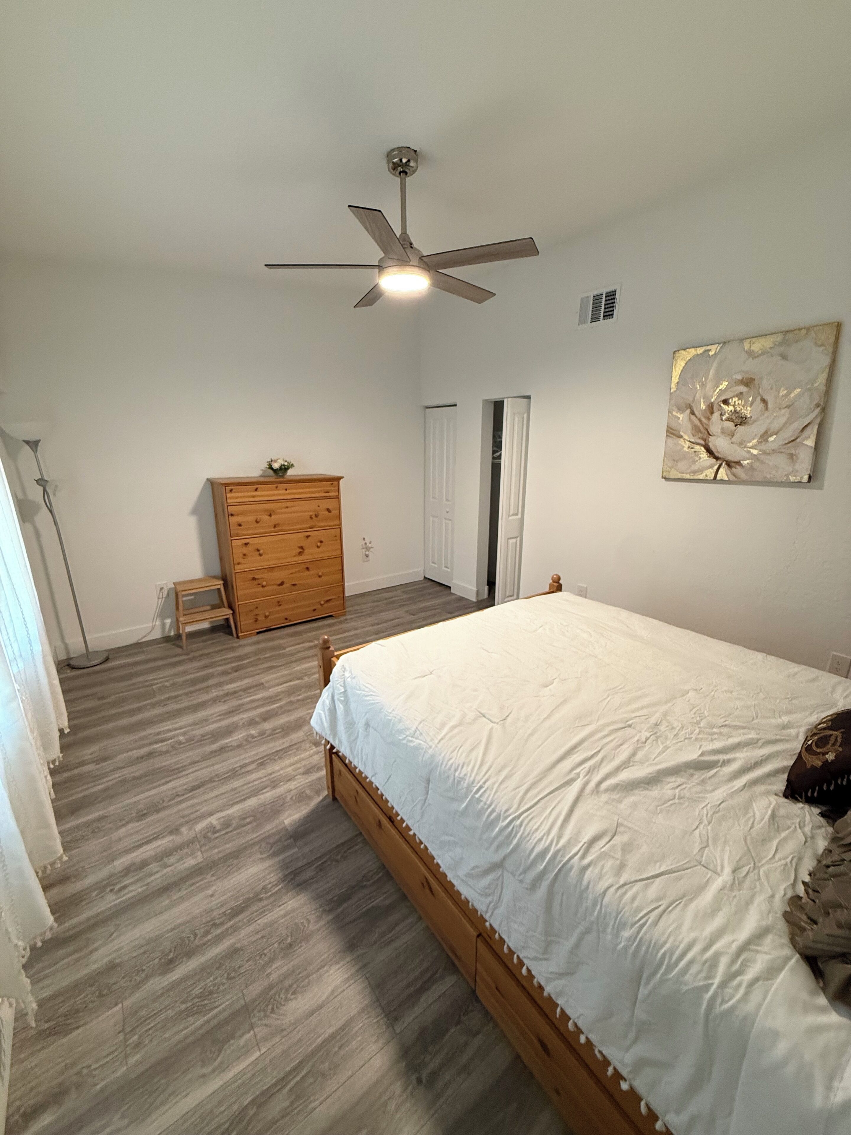 A bedroom with a wooden bed, a ceiling fan, a dresser, and a door.