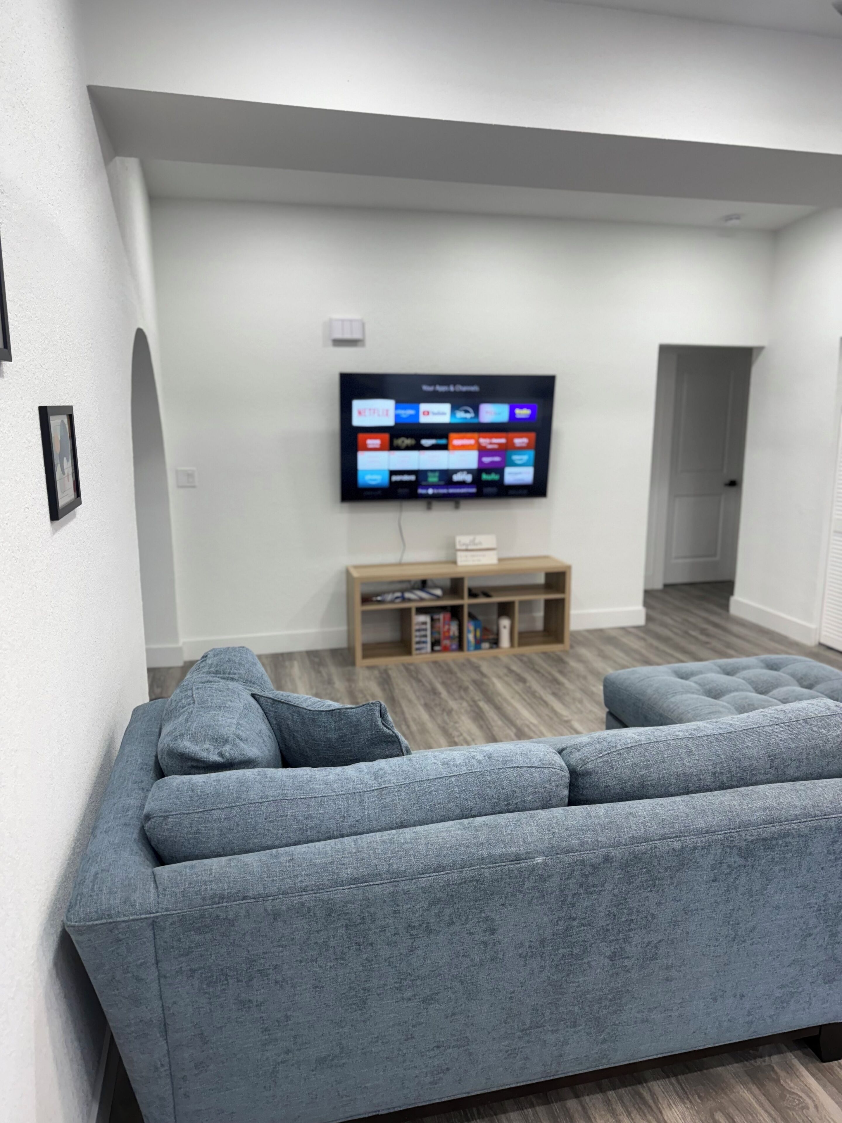 Ett vardagsrum med en grå hörnsoffa, en platt-TV som är monterad på väggen och en träinredd TV-möbel under.