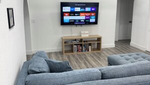 Ein Wohnzimmer mit einem grauen Ecksofa, einem an der Wand montierten Flachbildfernseher und einer Holzunterhaltungseinheit darunter.