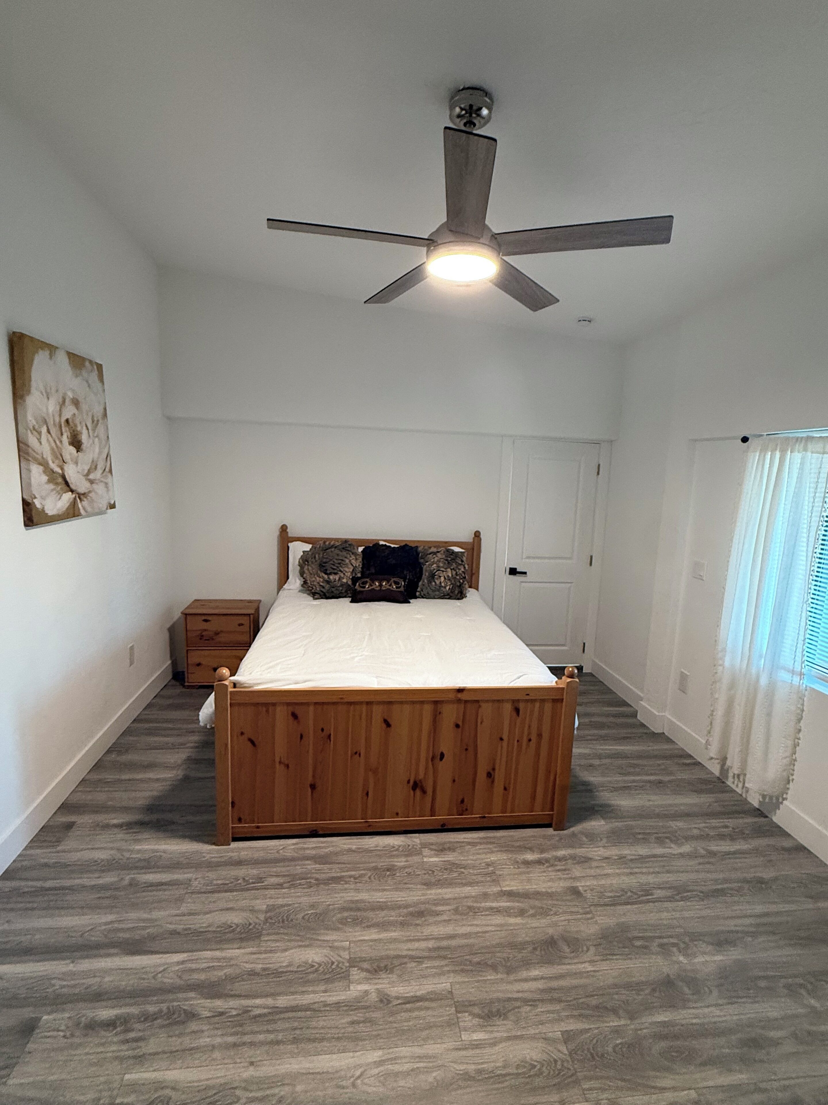 Une chambre à coucher avec un lit en bois, un ventilateur de plafond, une table de chevet et une porte.