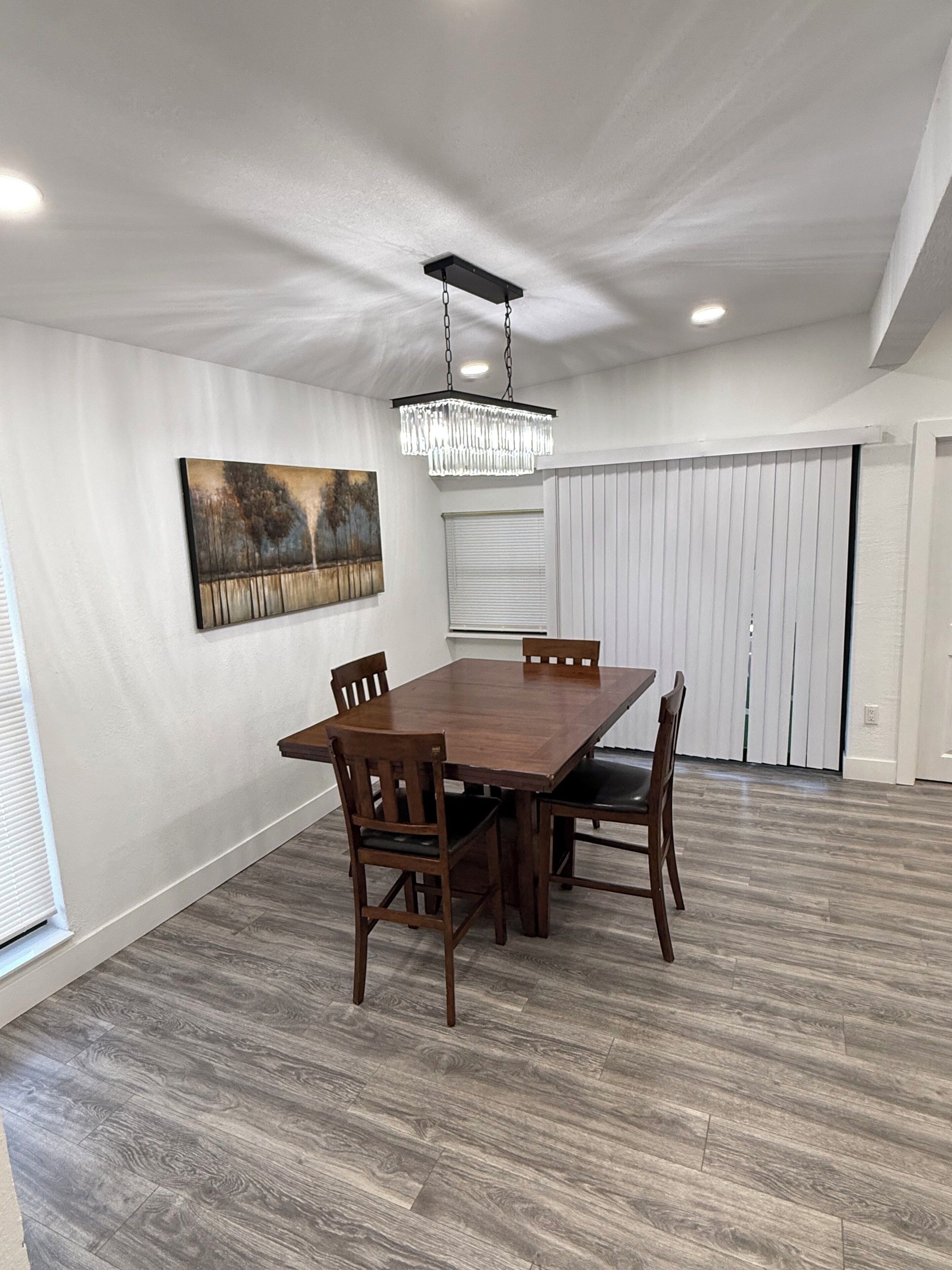 Un coin repas avec une table et des chaises en bois, un lustre, un tableau au mur et une porte coulissante.