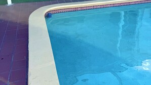 Ein Pool mit Fliesenbord, ein Deckenventilator und eine Sitzecke mit zwei Stühlen und einem Tisch.