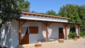 A small white building with a tiled roof, wooden beams, and a covered porch with chairs and planters. - Il Poggetto di Barbara - Casa Bianca (Scansano)