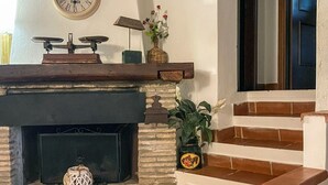 A fireplace with a clock above it, a small table with a lamp, and a staircase with a potted plant. - Il Poggetto di Barbara - Casa Bianca (Scansano)