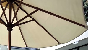 A modern outdoor lounge area with two cushioned chairs and a large umbrella, overlooking a swimming pool and a glass-enclosed dining area. - Lovely 2-bedroom villa with AC in beautiful Ubud Bali (Bali)