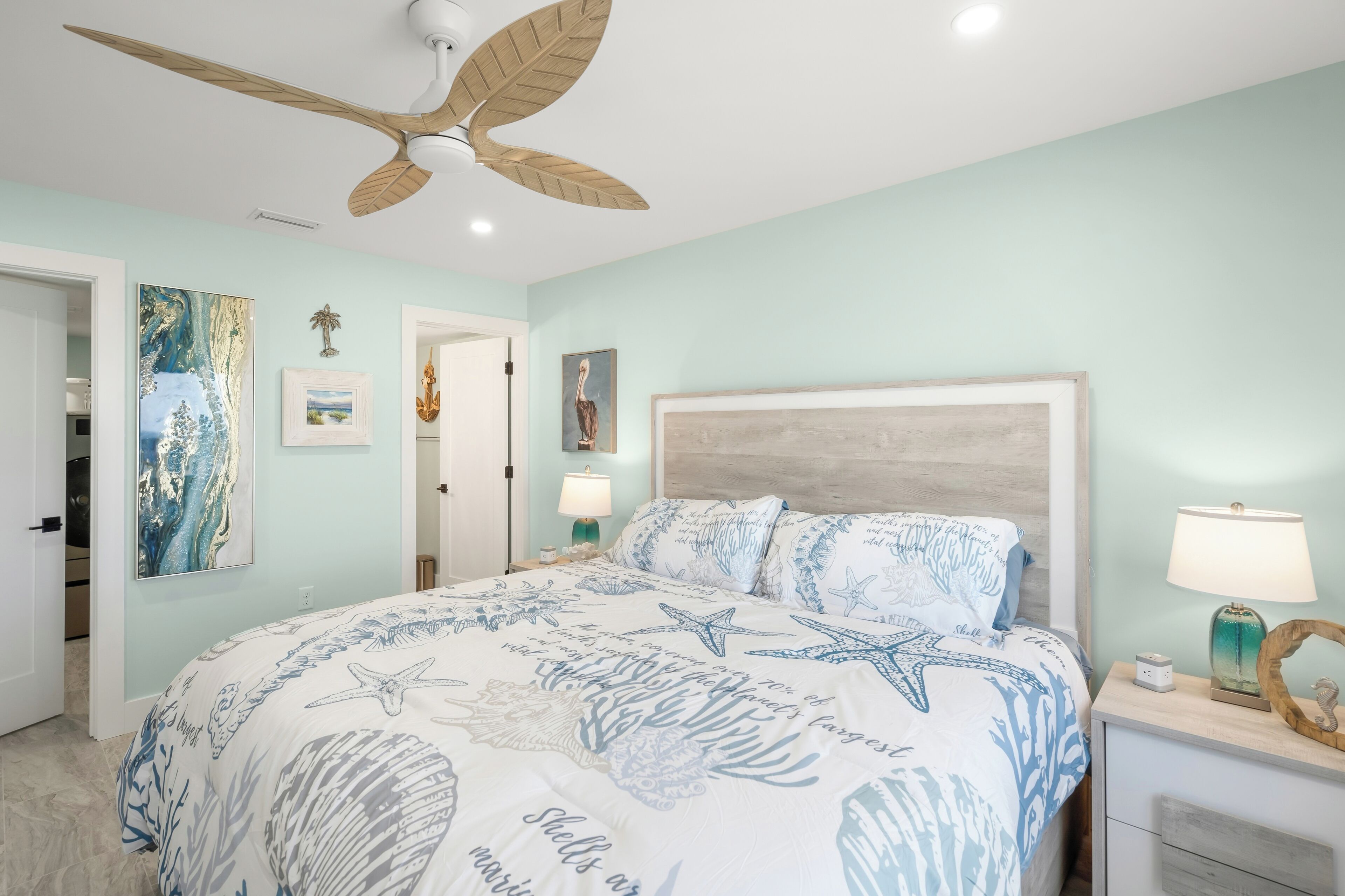Une chambre à coucher avec un lit agrémenté d’une couvre-lit sur le thème de la marine, un ventilateur de plafond et une table de chevet avec une lampe.