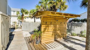 Una estructura de madera con listones horizontales, una terraza de madera y suelo arenoso.