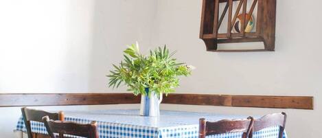 Un coin repas rustique avec une nappe à carreaux, des chaises en bois, une plante en pot, un luminaire suspendu et un buffet en bois.