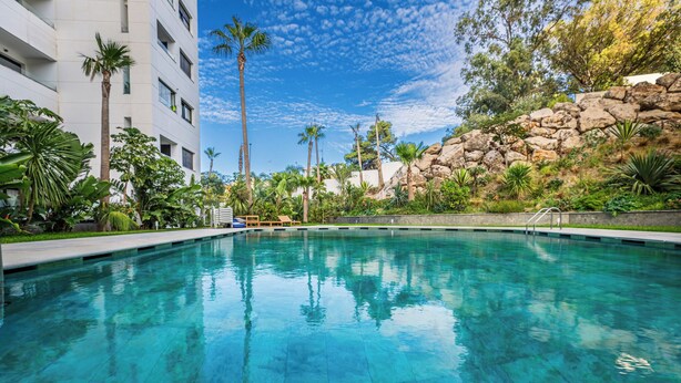 Una piscina cristalina rodeada de exuberante vegetación y una ladera rocosa.