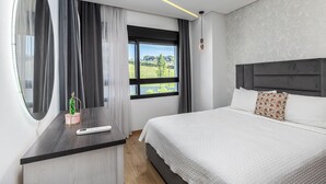Un dormitorio moderno con una cama grande, una mesita de noche, un espejo y una ventana con vistas a zonas verdes.