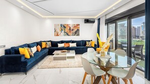 Una sala moderna con un sofá seccional azul oscuro, una mesa de centro de vidrio y un comedor con mesa y sillas de vidrio.