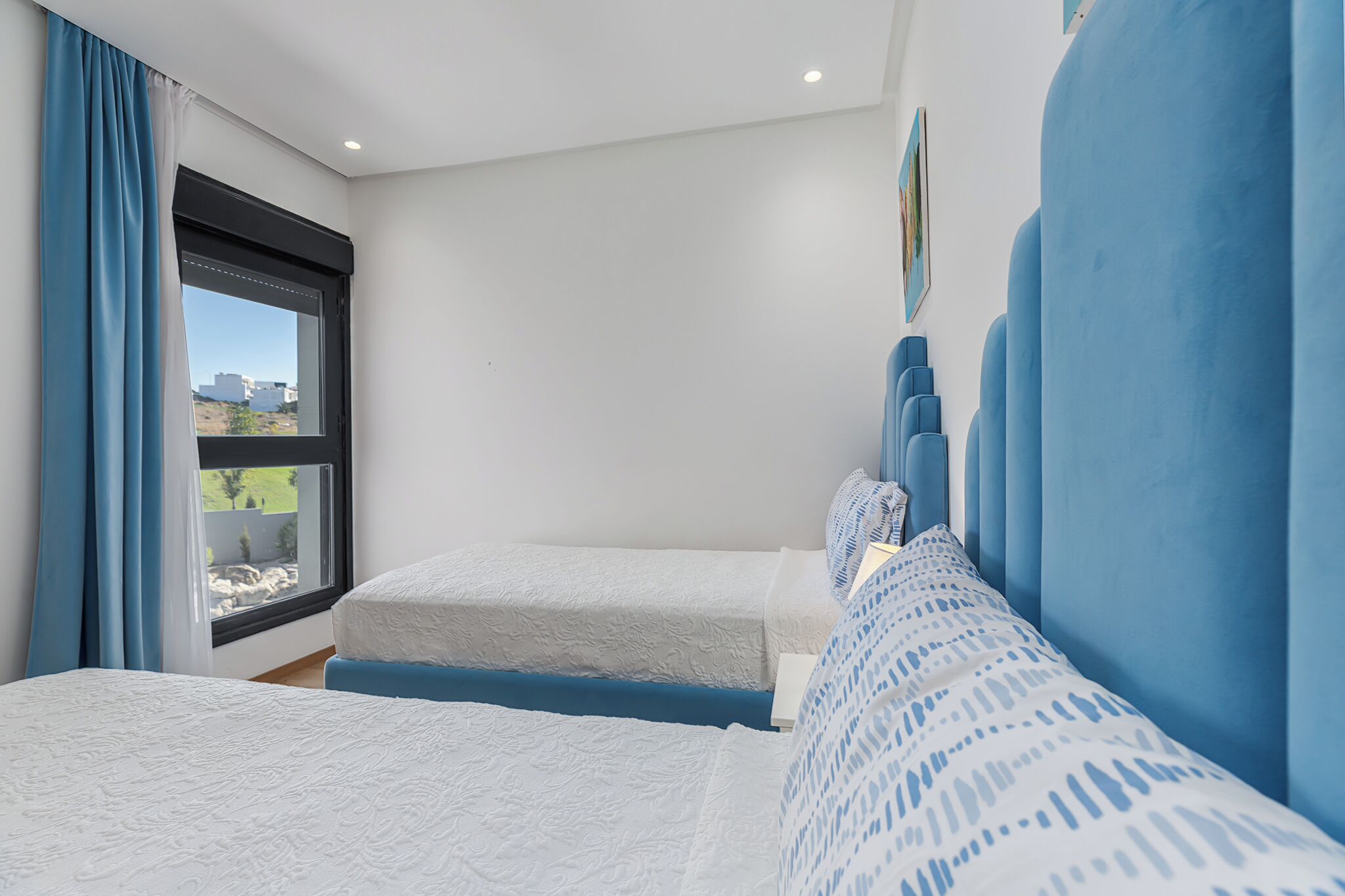 A bedroom with two beds, a window with a view, and blue curtains.