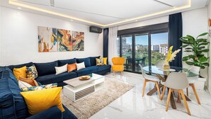 Una sala de estar moderna con un sofá azul, una mesa de centro de vidrio y un comedor con una mesa y sillas de vidrio.