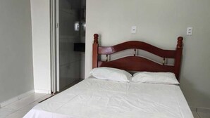 A single-bed room with a wooden headboard, white bedding, and a sliding glass door leading to a bathroom. - Criptos Hotel e Restaurante (Várzea Grande)