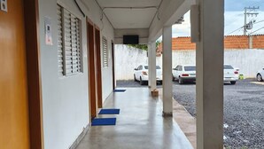 A corridor with a covered walkway, blue mats at the entrance of doors, and a view of parked cars outside. - Criptos Hotel e Restaurante (Várzea Grande)