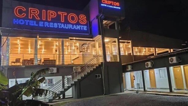 A hotel named 'CRIPTOS HOTEL ERESTAURANTE' with a modern facade, outdoor seating area, and a staircase leading to the entrance. - Criptos Hotel e Restaurante (Várzea Grande)