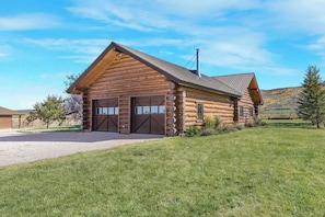 A log cabin with two garage doors, a chimney, and a grassy yard. - Teton Homestead: Log Cabin on 4 Acres w/ Hot Tub (Driggs)
