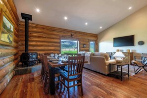 A log cabin interior with a dining table, chairs, a sofa, a TV, and a fireplace. - Teton Homestead: Log Cabin on 4 Acres w/ Hot Tub (Driggs)