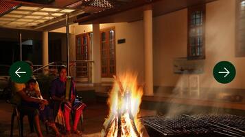 A building with a covered outdoor seating area, a grill, and a fire.