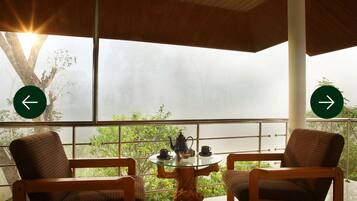 A balcony with two wooden chairs, a glass table, and a teapot.
