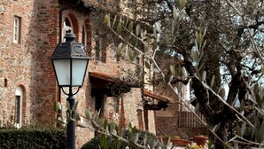 A traditional brick building with a stone facade, a wrought iron lamp post, and surrounding vegetation. - Borgo di Erboli (Cavriglia)