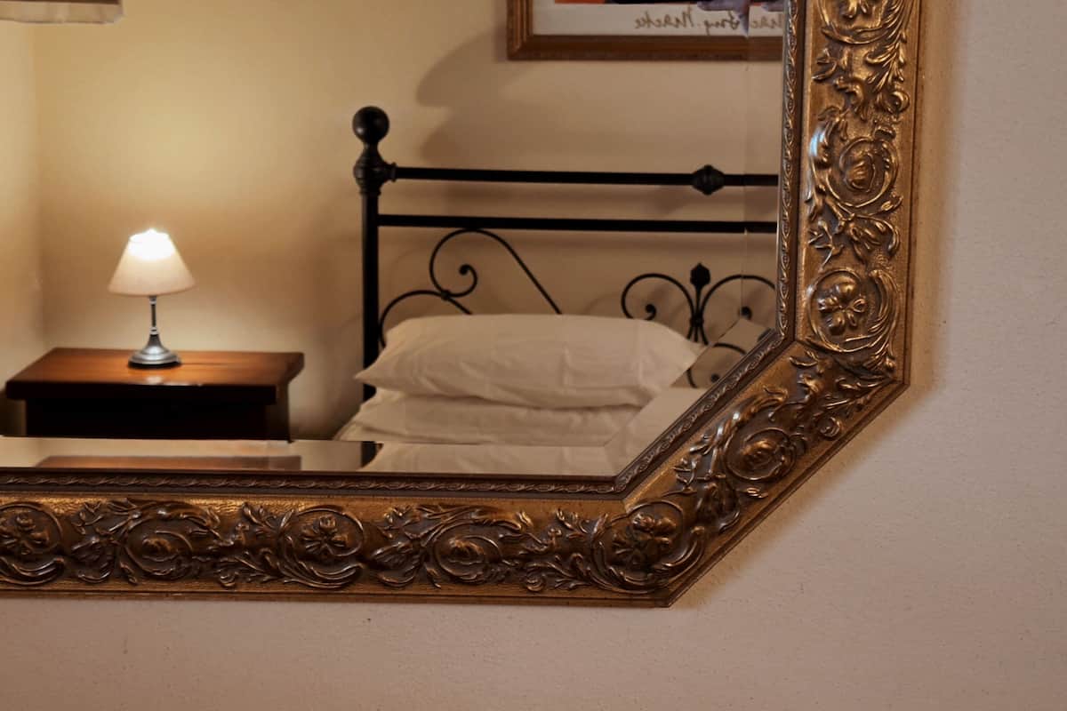 A bedroom with a bed, a bedside table with a lamp, and a large ornate mirror.