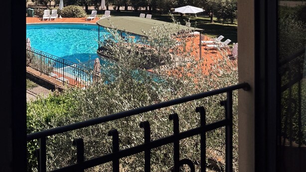 A view of a swimming pool with lounge chairs and umbrellas, surrounded by trees and hills. - Borgo di Erboli (Cavriglia)