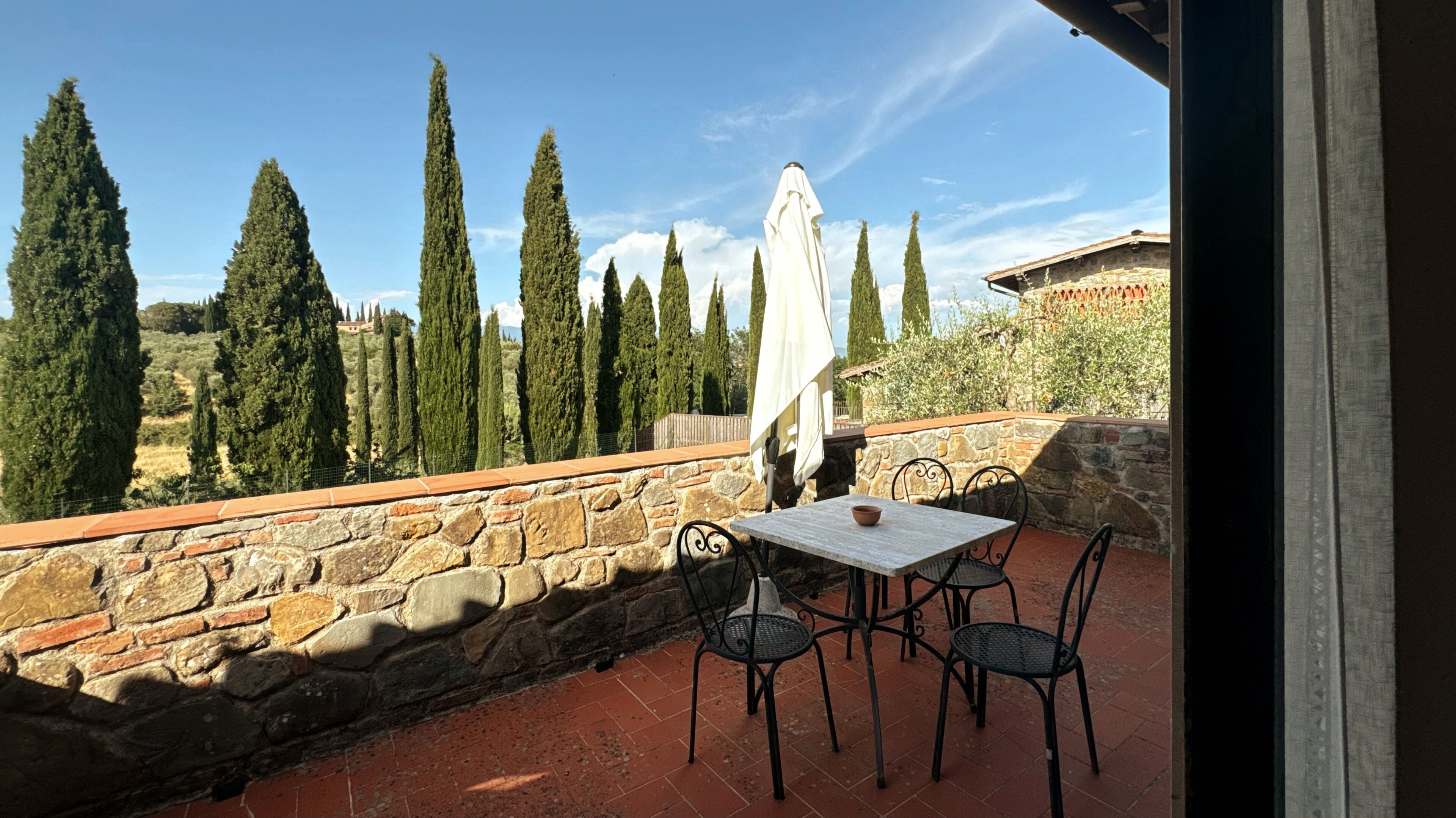 Un patio con paredes de piedra, una mesa, sillas y un paraguas blanco.