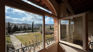 A room with a large window offering a view of a landscaped garden, a pergola, and distant mountains. - Borgo di Erboli (Cavriglia)