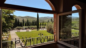A balcony with a view of a manicured lawn, seating area, and distant hills. - Borgo di Erboli (Cavriglia)
