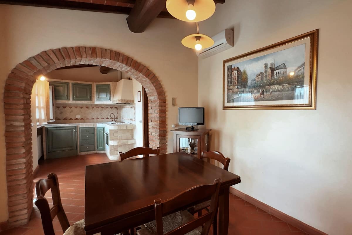 A dining area with a table and chairs, a television, and a painting on the wall.