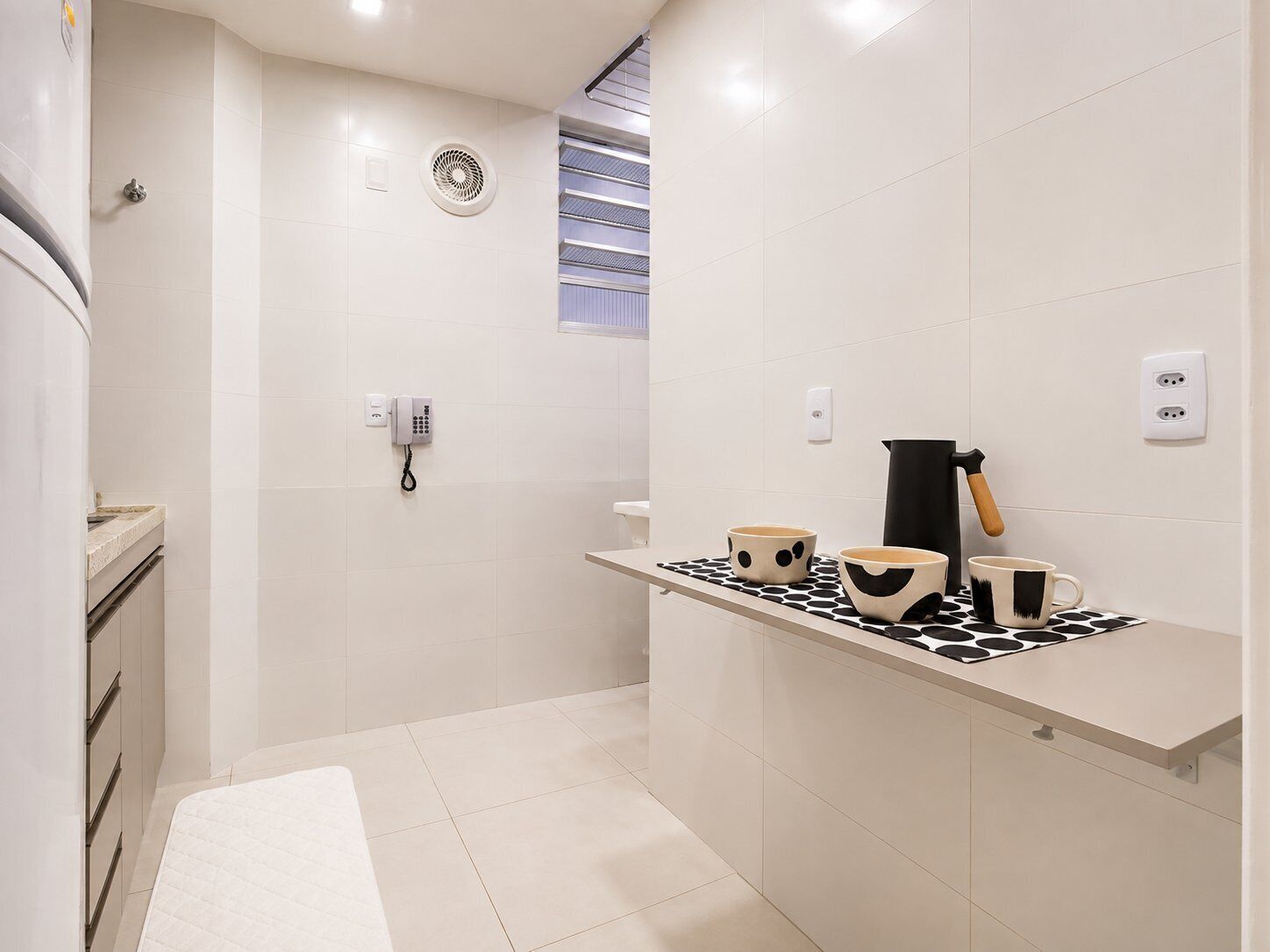A modern bathroom with a toilet, a shower, and a sink. There is a telephone mounted on the wall and a towel rack.