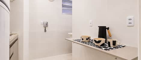 A modern bathroom with a toilet, a shower, and a sink. There is a telephone mounted on the wall and a towel rack.
