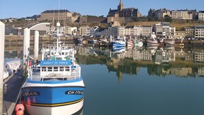 Un puerto con una embarcación azul y blanca de gran tamaño amarrada al muelle, rodeado de aguas tranquilas que reflejan los edificios y estructuras cercanas.