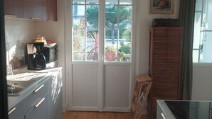 Una cocina con suelo de madera, armarios blancos, una cafetera y un ventanal con vistas al exterior.