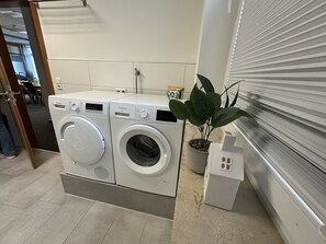 A laundry area with two front-loading washing machines, a potted plant, and a white storage unit. - Bordinghouse Halverde (Hopsten)