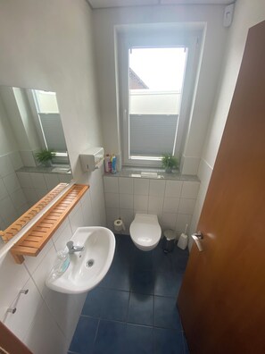 Ett litet badrum med ett vitt handfat, en toalett, ett fönster och en spegel.