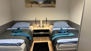 Une petite chambre, de taille modeste, avec deux lits simples, une table de chevet avec une lampe et un tableau accroché au mur.