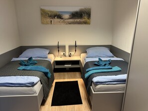 A small, compact room with two single beds, a nightstand with a lamp, and a painting on the wall. - Bordinghouse Halverde (Hopsten)