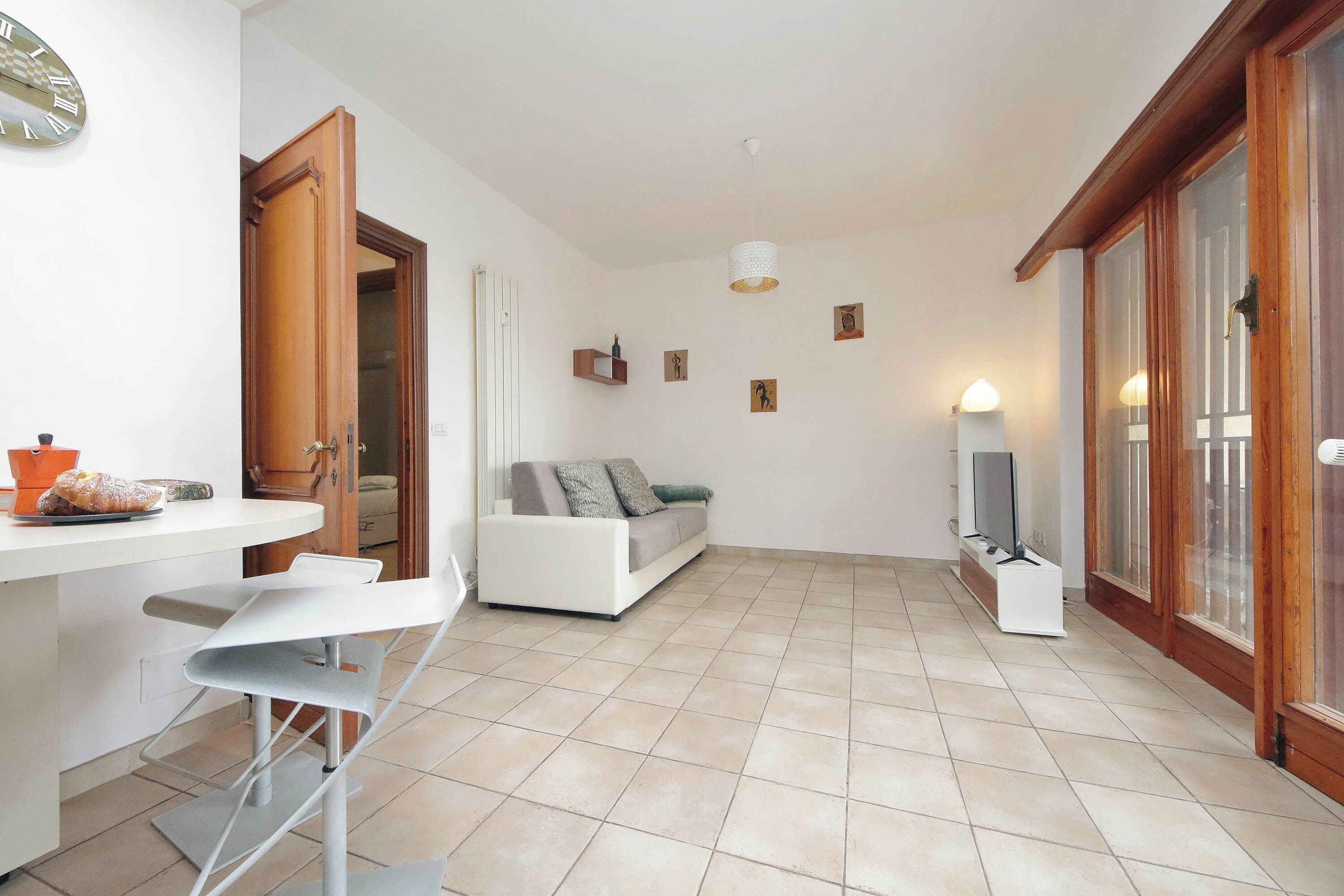 Amplia sala de estar con un sofá blanco, una mesa de comedor con sillas, un televisor y un reloj en la pared.