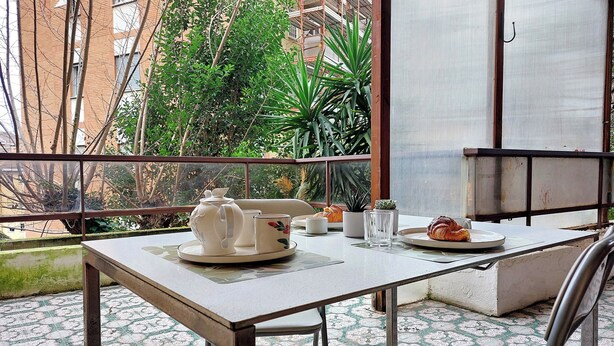 Ein Balkon mit einem Tisch, gedeckt für das Frühstück, darunter ein Croissant, ein Teekessel und Tassen.