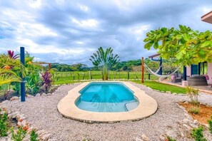 A swimming pool surrounded by a garden with various plants and a hammock.